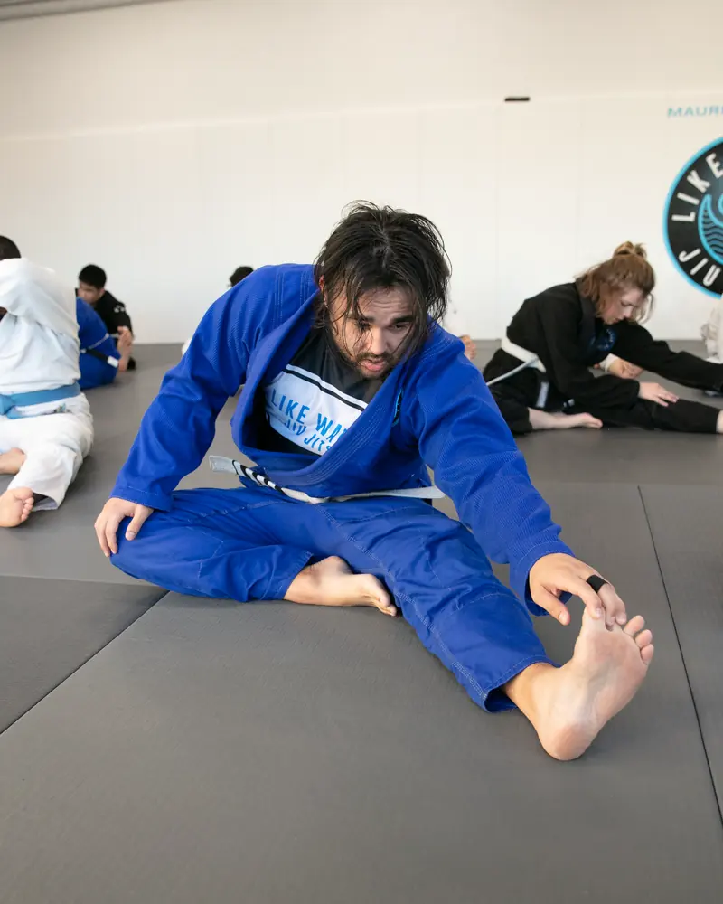 A student in a blue gi stretching on the mat during the warm-up