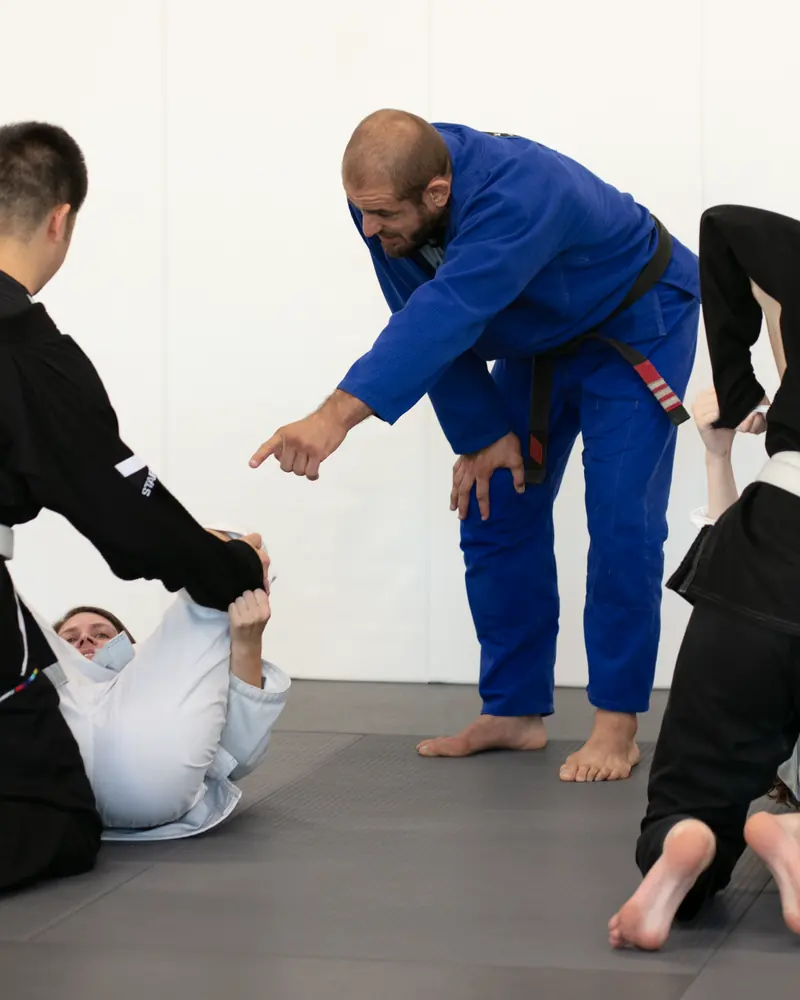 A coach in a blue gi pointing out a detail to a student on the mat